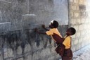 Two boys are looking at the draws of one of the projects in a blackboard, in a street  of the Ghanaian village of Azizakp